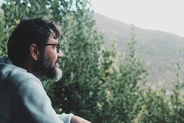 Side portrait view of mature man with beard and glasses looking the nature woods in background. Male people enjoying green garden and forest landscape. Concept of people and outdoor leisure activity