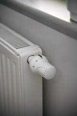 Close-up of turning down the thermostat on a radiator to save energy due to heating cost price hike. Concept of economizing cost during cold weather and energy crisis.