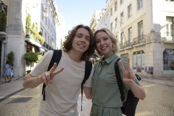 Joyful tourist couple making peace gesture. Man and woman smiling, looking at camera. Portrait, travelling concept