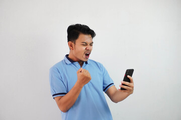 excited or happy portrait young asian man holding phone with clenched fists wearing blue polo t...