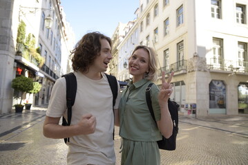 Fototapeta premium Happy tourist couple walking. Man and woman travelling, talking, woman showing peace sign. Portrait, travelling concept