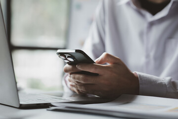 Business man looking at financial information from a mobile phone, he is checking company financial documents, he is an executive of a startup company. Concept of financial management.