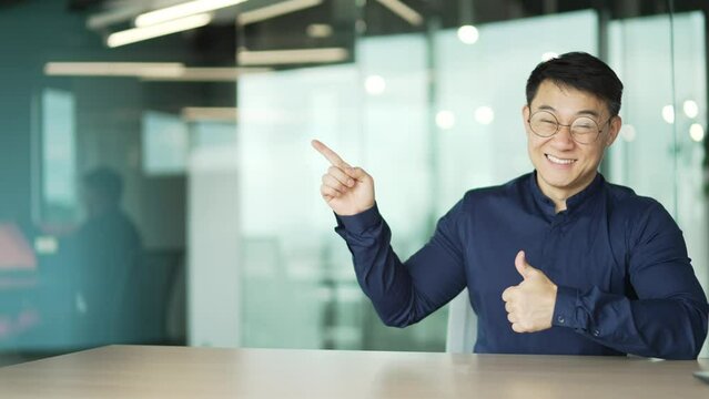Portrait of successful asian businessman IT programmer with glasses showing at empty copy space for text recommend good promotional sale offer at modern glass office indoor Template for advertising