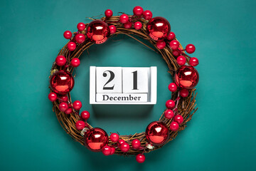 Christmas wreath decorated with red berries, wooden calendar date 21 December isolated on green background Concept of Christmas preparation, atmosphere Wishes card Hand made Christmas wreath Flat lay