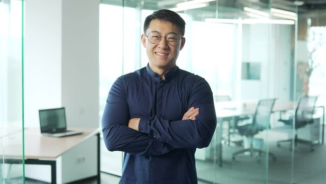 Portrait of smiling IT specialist programmer with glasses looking at the camera in modern office centre Asian entrepreneur professional developer man with crossed arms in development company indoors