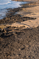 Sunrise on the beach on a summer day. Shore, rocky beach. Textures of the stones on the shore. Ocean waves in the background. Calm clear sky, orange color. El medano, Tenerife, Canary Islands, Spain.