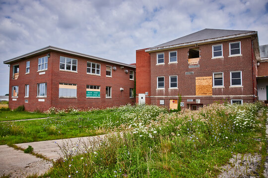 Three story abandoned brick buildings with overgrowth and boarded up windows