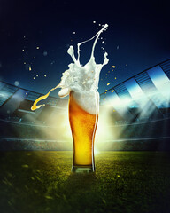 Foamy splashes. Mug with lager chill beer on grass at football stadium over evening sky with...