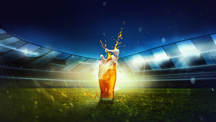 Glass with lager foamy beer on grass at football stadium over evening sky with flashlights. Game...