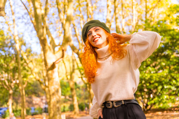 Portrait of red-haired woman with beret in a park, forest at sunset, lifestyle smiling