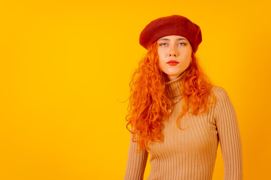 Portrait of red-haired woman in a red beret on a yellow background, studio shot