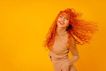 Red-haired woman on a yellow background, studio shot, moving her hair and with frozen hair