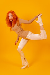 Fototapeta na wymiar Red-haired woman on a yellow background, studio shot, fashion posed, full body in white boots