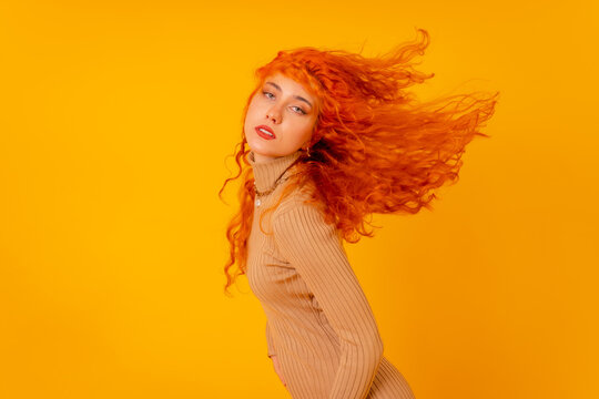 Red-haired woman on a yellow background, studio shot, moving her hair and with frozen hair