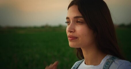 Portrait of a Beautiful Young Female Standing in Rural Field, Stroking Her Hair and Looking into the Distance. Smiling Brunette with Authentic Facial Features and Green Eyes. - Powered by Adobe