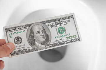 Hand throwing hundred dollar down the toilet.