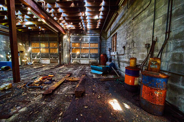 Messy abandoned interior of mechanic shop with garage doors and rusted barrels