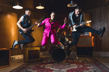 Full-length indoor shot of music band jumping. Lead singer and two guitarist jump in the air....