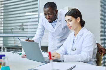Portrait of young woman using laptop in medical laboratory with chief scientist