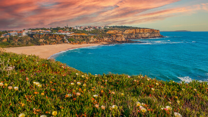  Small European town against cloudy sunset sky, sandy beach and Atlantic Ocean. Beautiful landscape of  rocky ocean coastline with flowering succulents.  Beautiful natural beauty.  Portugal.