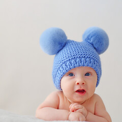 A happy newborn baby in a blue hat with pompoms looks into the camera. A smiling two-month-old infant is lying on a blanket. Beautiful, happy little child with blue eyes.  Cheerful White kid. .