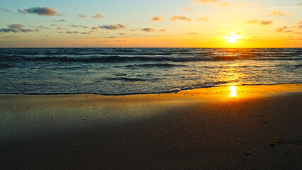 Beautiful sandy beach while sunset. Beautiful seascape of a sandy beach. Sun over horizon and  rolling ocean waves to the shore while sunset. Summer, travel and tourism. Beautiful wild nature.