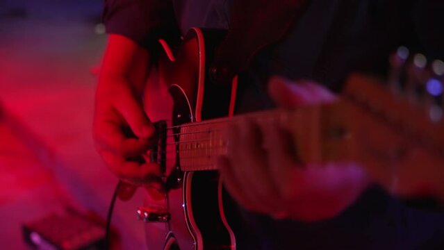 Stage lights flash across electric guitar as male guitarist strums chords during music concert, red lighting slow motion close up 4K