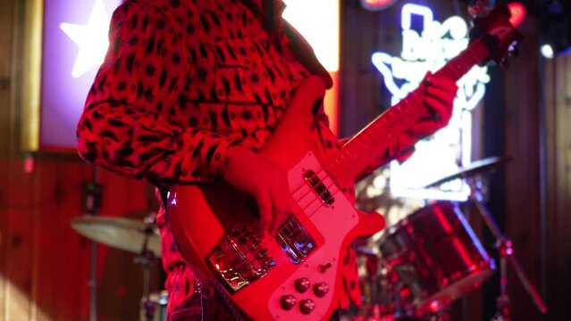 Male guitarist plays electric bass guitar on stage in band, red lighting slow motion 4K