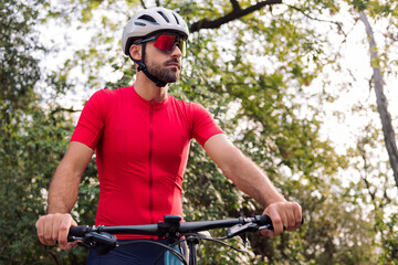 portrait of a young man in cycling clothes with his mountain bike in the middle of the forest,...