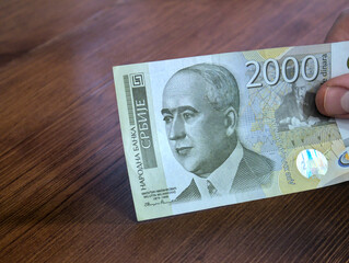 A close-up shot of a 2000 Serbian dinar banknote. A person holds a banknote in his hand