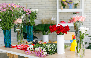 Closeup studio shot fresh red and pink petal roses bunch bouquet in white ceramic vase placed on workshop table with other colorful flowers material for florist decorating arranging in floral store