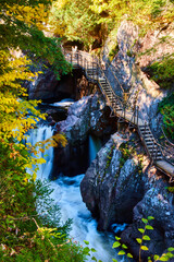 Fototapeta premium Boardwalk steps built into rocky cliffs of deep gorge with rapids, waterfalls, and fall colors
