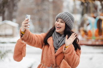 Happy long haired woman with amazing smile taking a video call  by phone at winter park