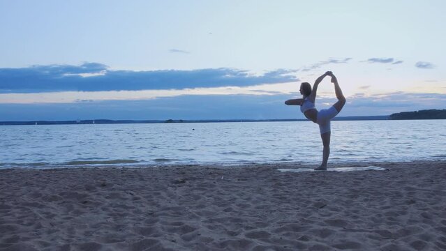 young woman performing a set of exercises near the lake. King dancer pose.