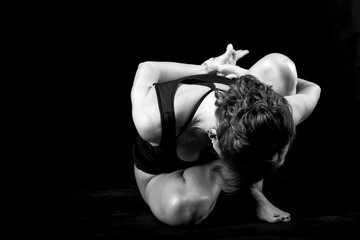 A young, slender, athletic, red-haired girl in a black T-shirt and black leggings sits in an asana...