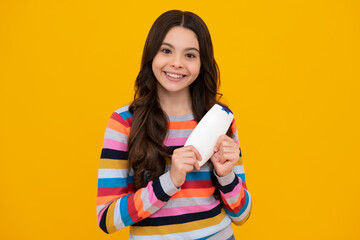 Teenager child girl showing bottle shampoo conditioners or shower gel isolated on yellow background. Hair cosmetic product. Mock up bottle. Happy teenager, smiling emotions of teen girl.