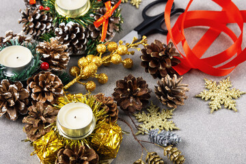 Set for making for Christmas decorations on the table from scissors, jewelry, satin ribbon, cones and candles on a wooden background