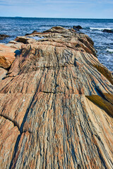 Layered sheet rocks like petrified wood on rocky coast of Maine lead to ocean