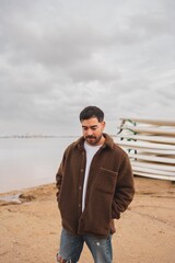 Caucasian young man by the lake in cloudy weather wearing winter clothing