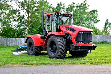 Obraz premium red and black agricultural tractor with big wheels isolated on green lawn with fence on background 
