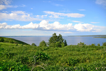 landscape with green hill and tree, river on horizon and white clouds on blue sky