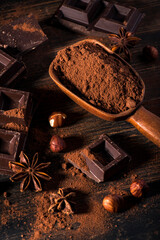 in the foreground, in a dark environment, cocoa powder, pieces of dark chocolate and hazelnuts - 553427821