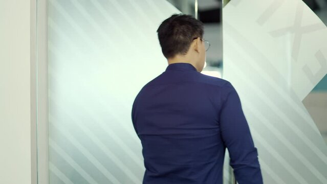 Successful young asian businessman with glasses open the glass office door in the modern business centre Confident employee IT specialist programmer entering meeting room at company alone indoors 