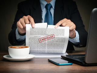 Businessman in a suit tearing up a canceled contract while sitting at the table - obrazy, fototapety, plakaty