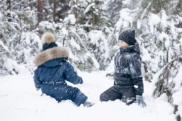 Fototapeta na wymiar Happy teenager and little boy playing in snow in winter forest. Children having fun snowball fight together outdoors. Christmas holidays and New year family vacation. Brothers walking in park