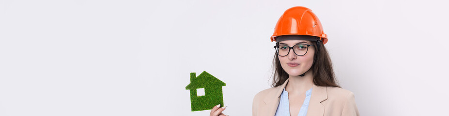 A girl in a construction helmet holds a green house. The concept of ecological clean housing.