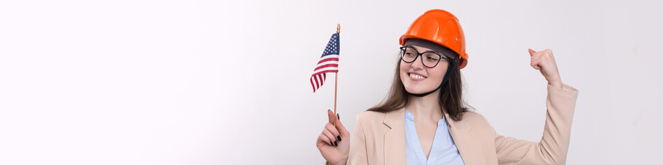 A girl in a construction helmet and an American flag stands happy on a white background.
