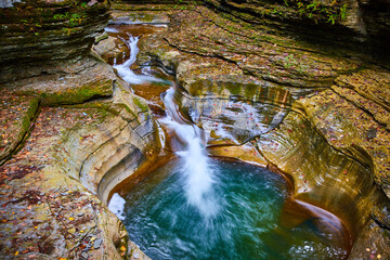Fall leaves cover terraced rocks in gorge with stunning blue water buckets and waterfalls