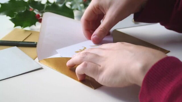 Close-up on the hands of a girl sending a thank you card in a golden envelope  to friends or family during the winter holidays, to express gratitude after receiving christmas gifts