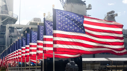 Line of American Flags patriotically waving in the breeze in front of US Navy ship